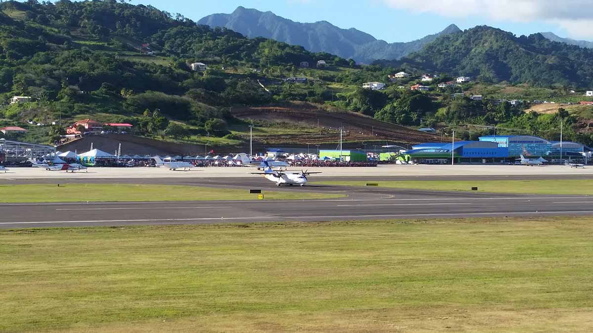 Photo of a small plane on airport runway with buildings and mountains in the background.